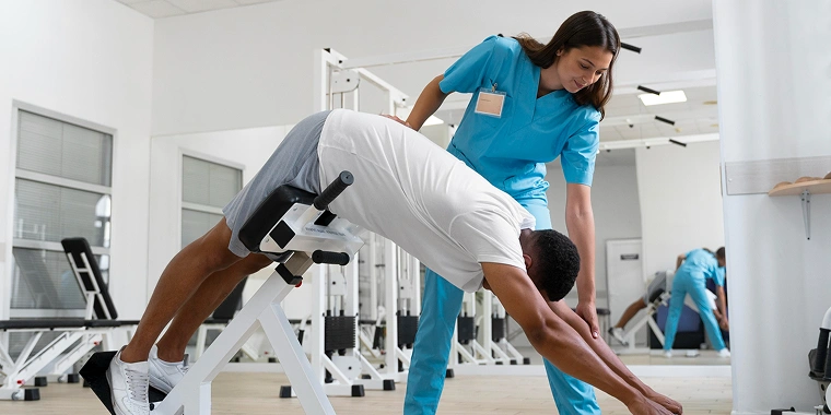A physical therapist assists a man stretching on a gym bench.