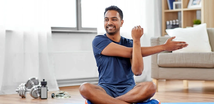 A man stretches his arm while sitting cross-legged on the floor.